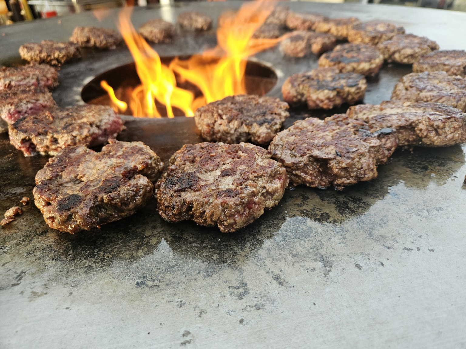 Frisch gegrillte Burgerpattys rund um das offene Feuer der Feuerplatte